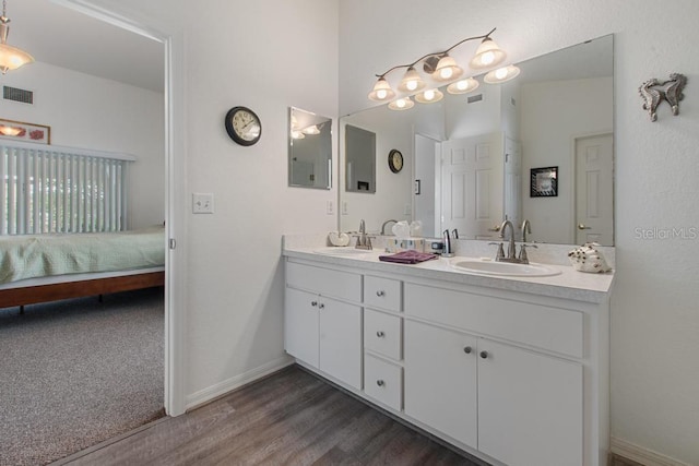 ensuite bathroom featuring baseboards, visible vents, a sink, and wood finished floors