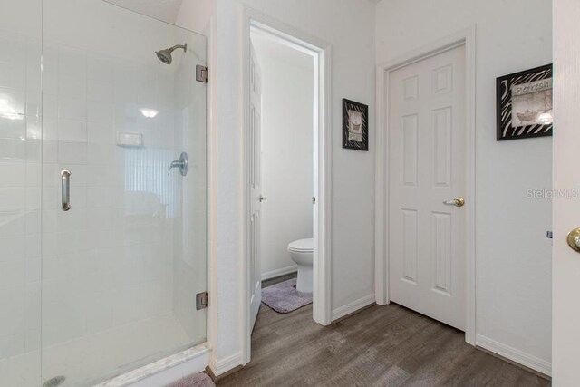 full bathroom with toilet, baseboards, wood finished floors, and a stall shower