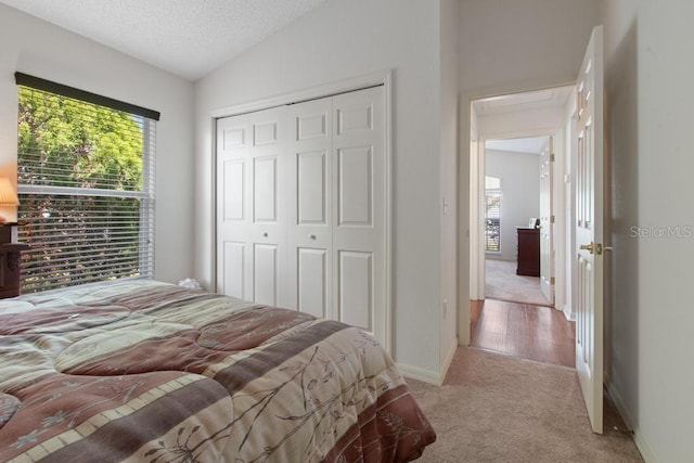 bedroom with a closet, carpet floors, a textured ceiling, baseboards, and lofted ceiling