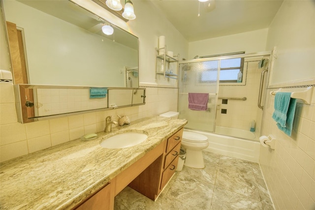 full bath with tile walls, toilet, vanity, wainscoting, and combined bath / shower with glass door