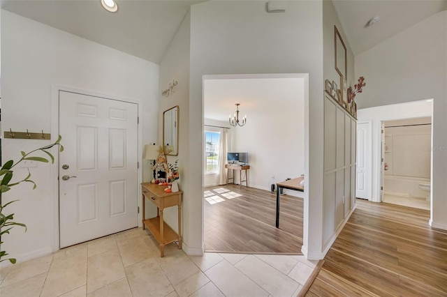 foyer featuring a notable chandelier, baseboards, light wood-style flooring, and high vaulted ceiling