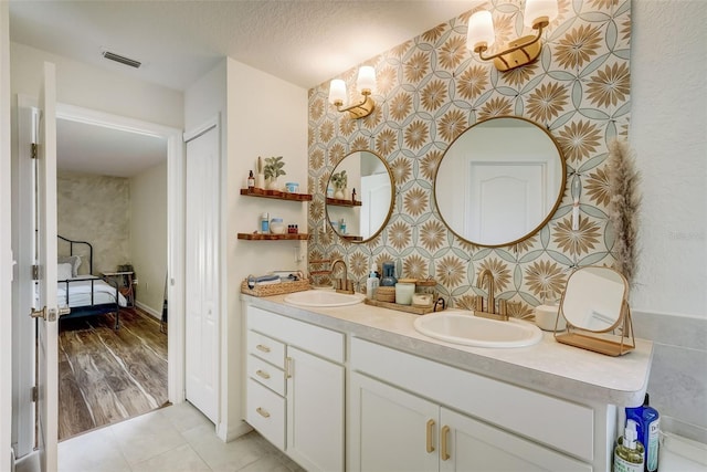 bathroom featuring double vanity, a textured ceiling, visible vents, and a sink