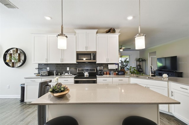 kitchen with appliances with stainless steel finishes, a sink, light wood finished floors, a kitchen breakfast bar, and backsplash