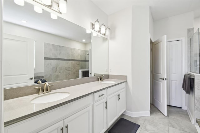 bathroom with double vanity, baseboards, a tile shower, and a sink