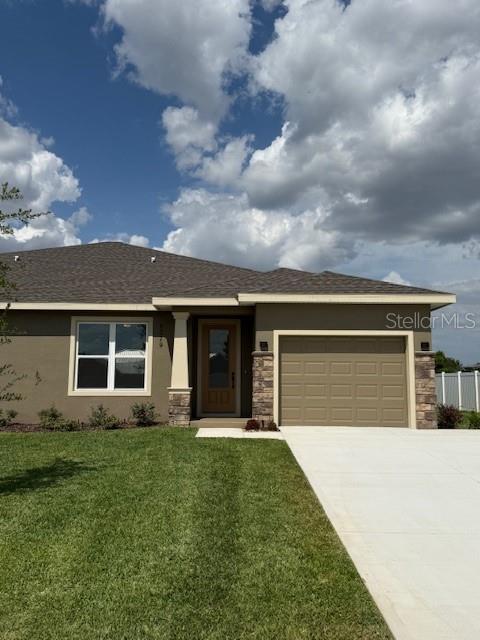 ranch-style house with a front lawn, concrete driveway, an attached garage, stone siding, and stucco siding