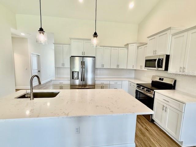 kitchen featuring appliances with stainless steel finishes, tasteful backsplash, a center island with sink, a sink, and white cabinets
