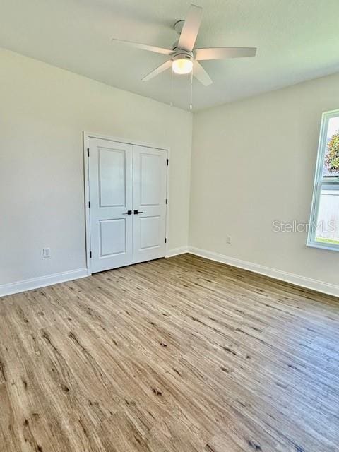 unfurnished bedroom featuring baseboards, ceiling fan, a closet, and wood finished floors