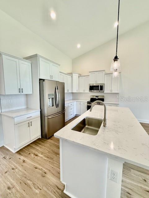 kitchen featuring hanging light fixtures, appliances with stainless steel finishes, a sink, light wood-style floors, and high vaulted ceiling