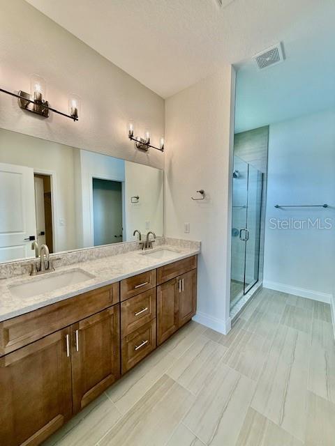 bathroom featuring visible vents, a sink, a stall shower, and double vanity