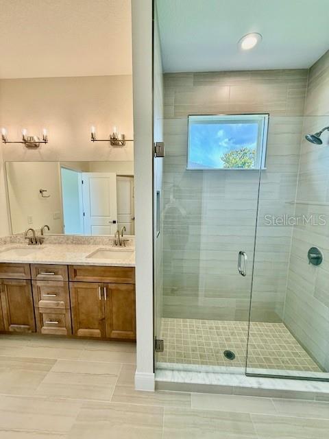 bathroom with double vanity, a sink, a stall shower, and tile patterned flooring