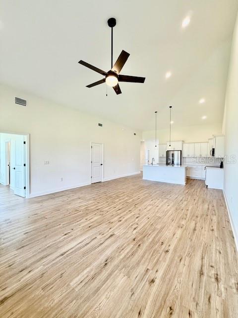 unfurnished living room with ceiling fan, visible vents, a sink, baseboards, and light wood-style floors