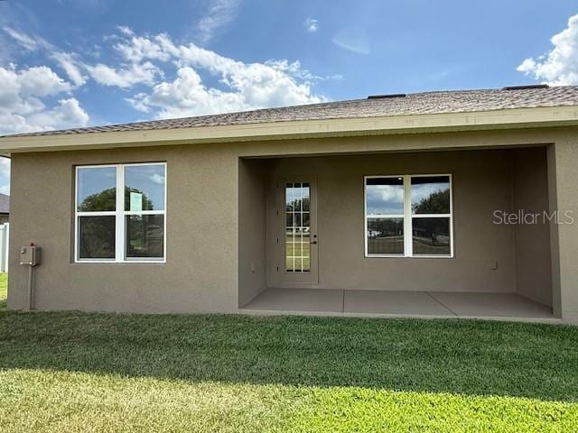 rear view of property with a lawn, stucco siding, and a patio area