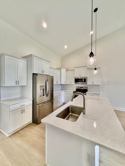 5275 Pebble Beach Dr, Sebring, FL 33872 - kitchen featuring a sink, stainless steel appliances, light wood-type flooring, vaulted ceiling, and a center island with sink