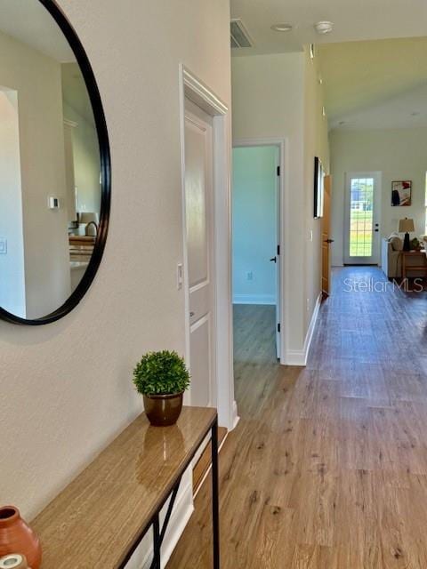 hall with visible vents, baseboards, and wood finished floors