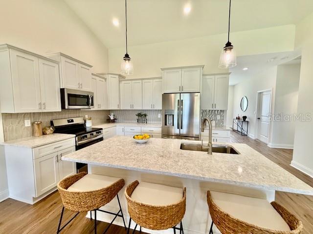 kitchen with a kitchen island with sink, a sink, light wood-style flooring, appliances with stainless steel finishes, and backsplash