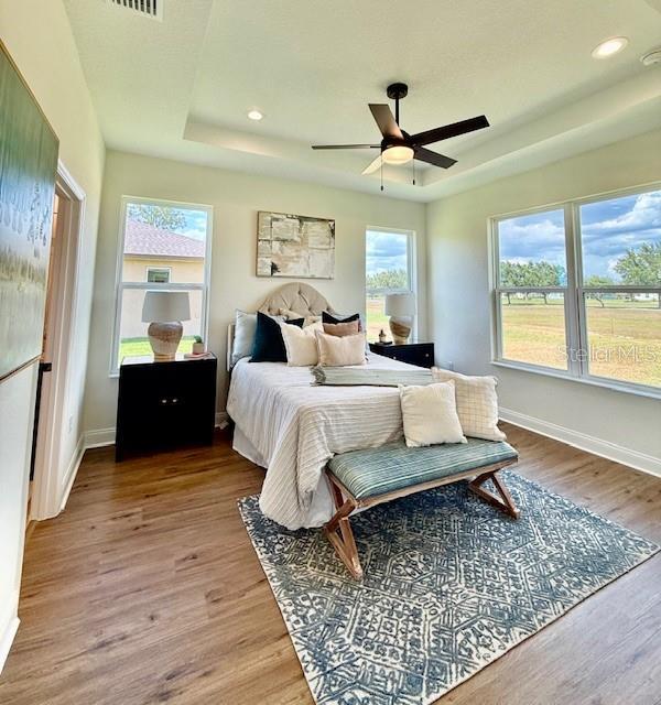 bedroom with baseboards, recessed lighting, a raised ceiling, and wood finished floors