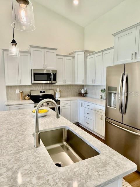 kitchen with decorative backsplash, light stone counters, a sink, appliances with stainless steel finishes, and hanging light fixtures