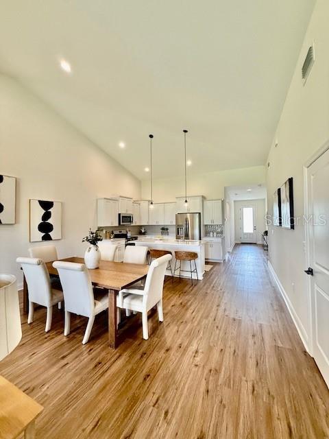 dining room featuring visible vents, light wood-style flooring, and high vaulted ceiling