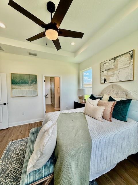 bedroom featuring a raised ceiling, a ceiling fan, baseboards, wood finished floors, and visible vents