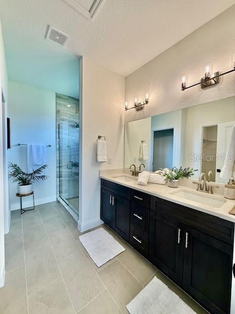 bathroom with a sink, tile patterned floors, a shower stall, and visible vents
