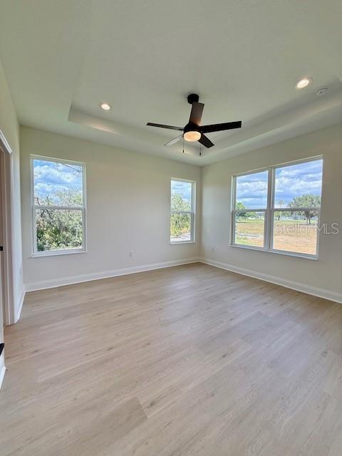 5273 Pebble Beach Dr, Sebring, FL 33872 - empty room with light wood-style floors, baseboards, a tray ceiling, and recessed lighting