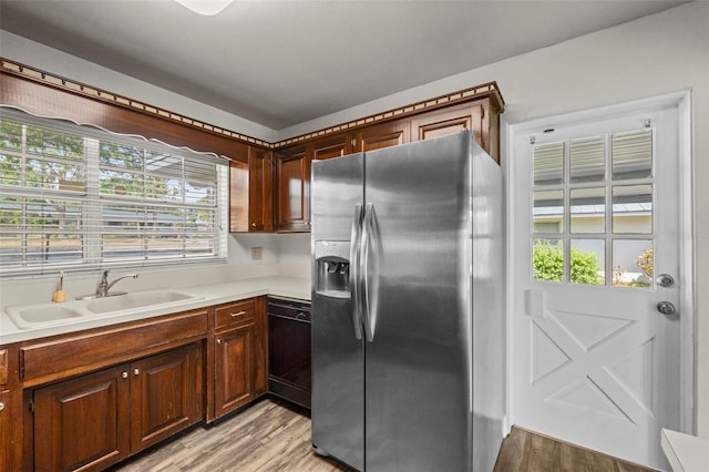 kitchen with dishwasher, light wood finished floors, a sink, stainless steel fridge, and light countertops