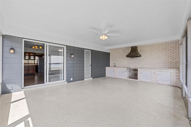unfurnished living room featuring speckled floor, ceiling fan, and brick wall