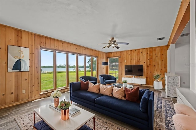 living area with wood walls, a ceiling fan, visible vents, and wood finished floors