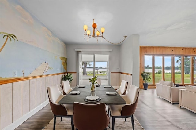 dining space with wainscoting, wooden walls, a water view, and a notable chandelier