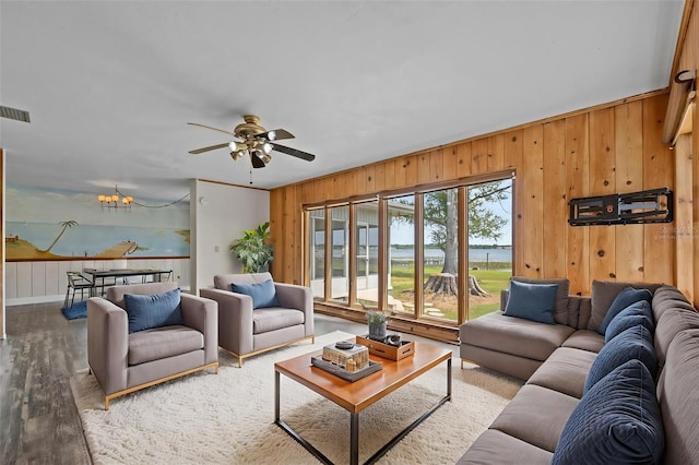 living area featuring wood walls, wood finished floors, ceiling fan with notable chandelier, and visible vents