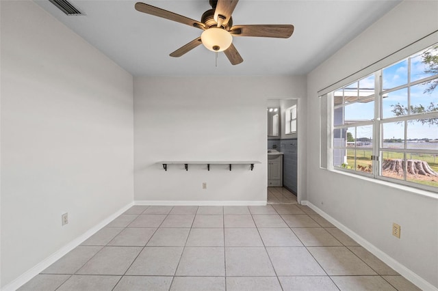 spare room featuring ceiling fan, a wealth of natural light, light tile patterned floors, and visible vents