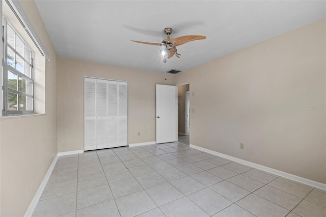unfurnished bedroom featuring a closet, light tile patterned floors, baseboards, ceiling fan, and visible vents