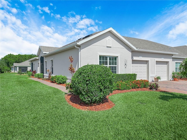 view of side of property featuring a lawn, driveway, a garage, stucco siding, and roof with shingles