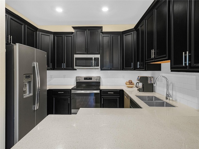 kitchen featuring dark cabinets, appliances with stainless steel finishes, a sink, and light stone countertops