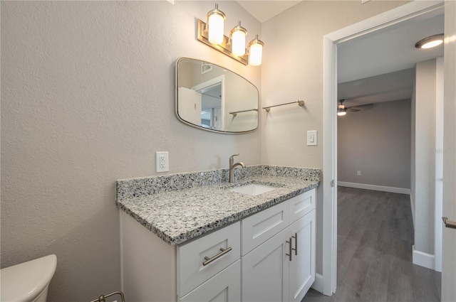 half bathroom with a ceiling fan, baseboards, toilet, vanity, and wood finished floors