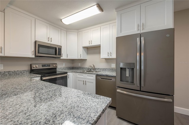 kitchen featuring light wood-style flooring, light stone counters, a sink, white cabinets, and appliances with stainless steel finishes