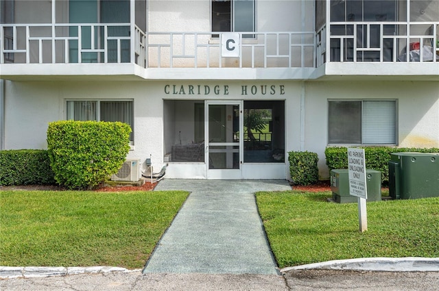property entrance with stucco siding, a lawn, and ac unit