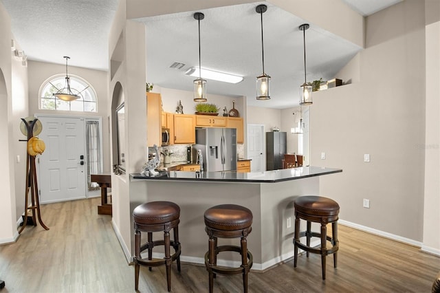 135 Minniehaha Cir, Haines City, FL 33844 - kitchen featuring stainless steel appliances, light brown cabinetry, arched walkways, light wood finished floors, and dark countertops