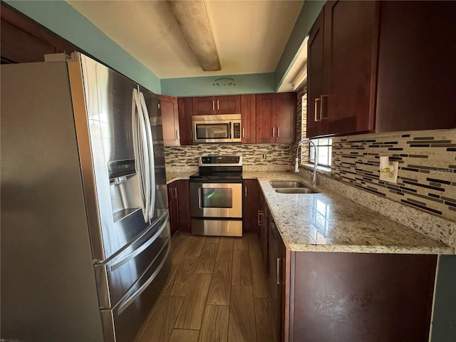 kitchen with stainless steel appliances, a sink, wood finish floors, backsplash, and light stone countertops