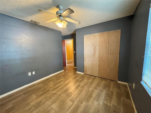 unfurnished bedroom with wood finished floors, a closet, baseboards, ceiling fan, and a textured ceiling