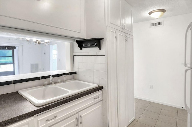 kitchen featuring a sink, white cabinetry, light tile patterned floors, dark countertops, and a textured ceiling