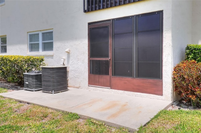 property entrance featuring stucco siding, central air condition unit, and a patio