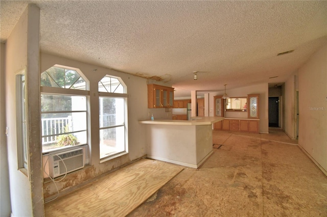 1294 1/2 38th St NW, Winter Haven, FL 33881 - kitchen featuring a textured ceiling, a peninsula, brown cabinetry, glass insert cabinets, and light countertops