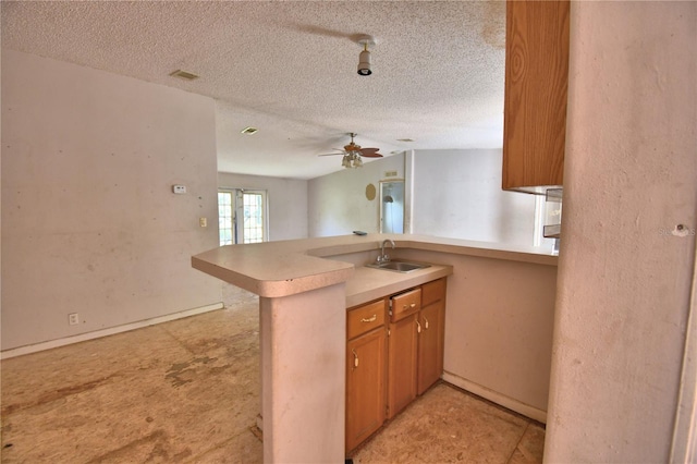 1294 1/2 38th St NW, Winter Haven, FL 33881 - kitchen featuring a sink, a peninsula, a ceiling fan, a textured ceiling, and brown cabinetry