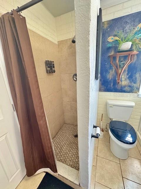 full bathroom featuring tiled shower, toilet, and tile patterned flooring