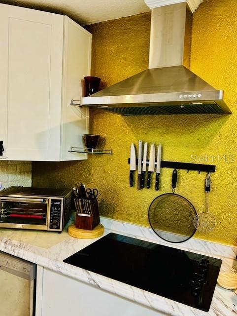 kitchen view of wall chimney exhaust hood, stainless steel dishwasher, white cabinets, backsplash, and a textured wall