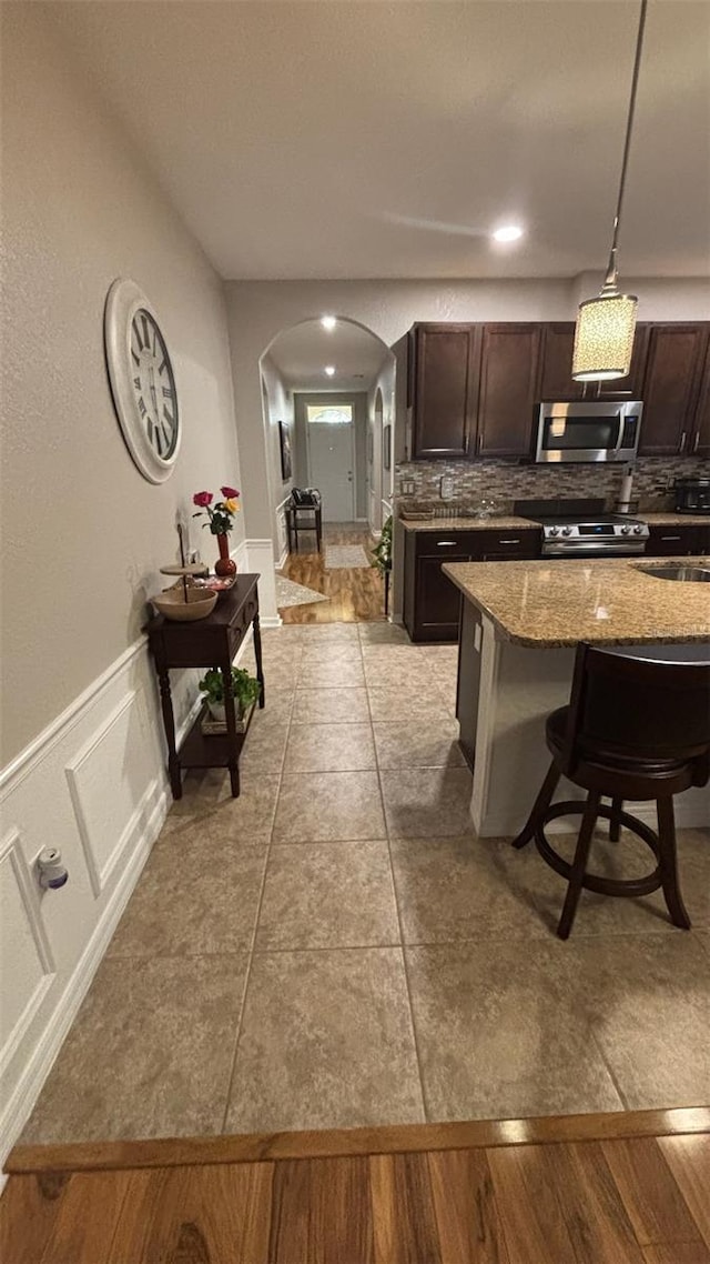 3828 Eloise Estates Ct, Winter Haven, FL 33881 - kitchen with appliances with stainless steel finishes, arched walkways, dark brown cabinetry, decorative backsplash, and stone countertops