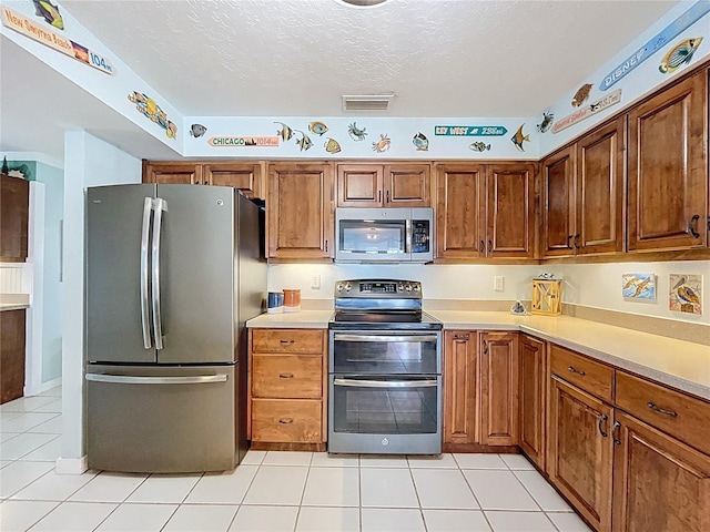255 Lake Link Rd, Winter Haven, FL 33884 - kitchen with stainless steel appliances, light tile patterned flooring, light countertops, brown cabinetry, and a textured ceiling