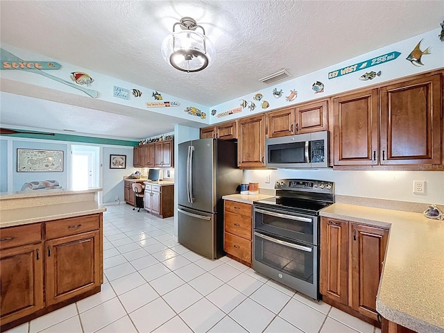 255 Lake Link Rd, Winter Haven, FL 33884 - kitchen with appliances with stainless steel finishes, light countertops, brown cabinetry, a textured ceiling, and light tile patterned floors
