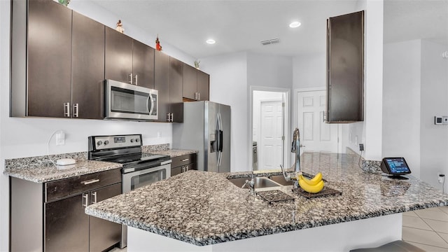 428 Aragosa Dr, Davenport, FL 33837 - kitchen with appliances with stainless steel finishes, a sink, a peninsula, dark brown cabinetry, and dark stone countertops